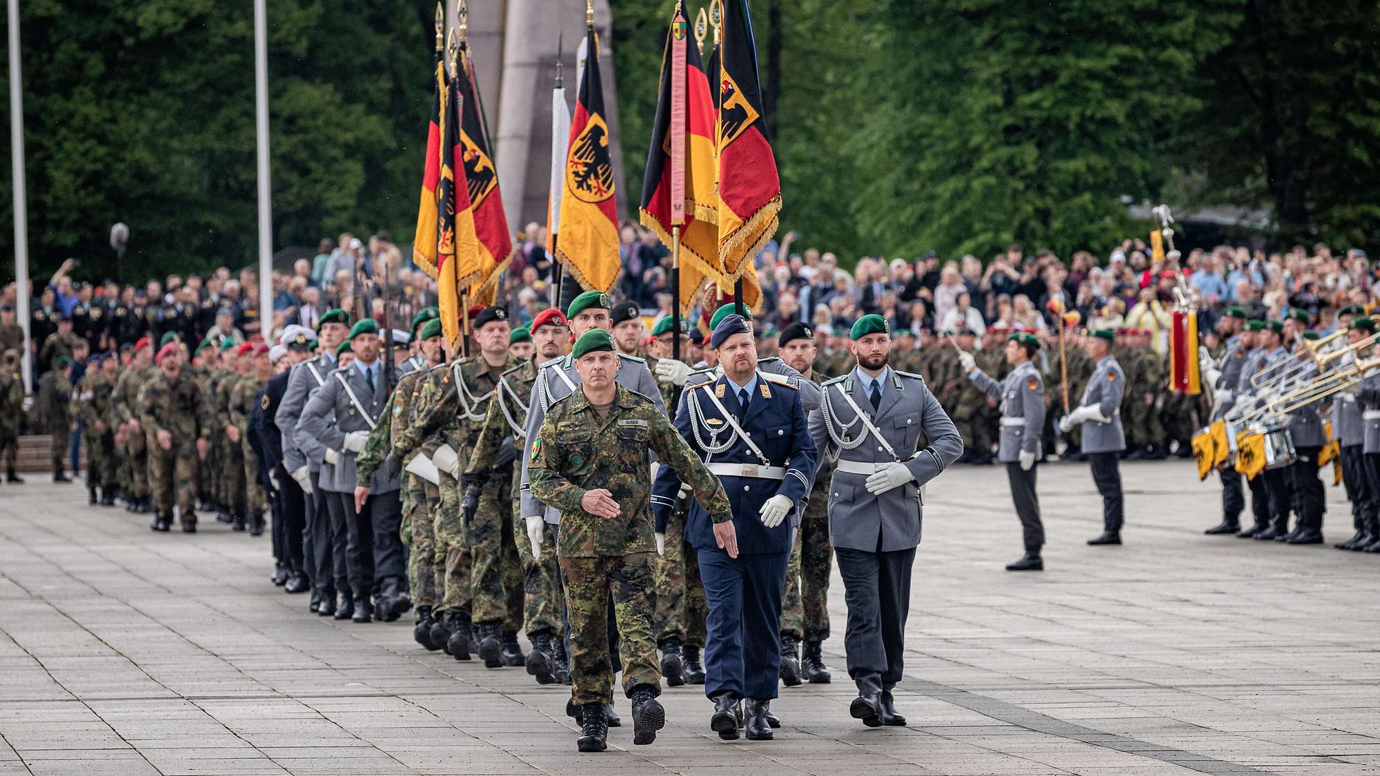 Mehrere deutsche Panzer fahren durch eine Stadt, litausche Soldaten salutieren am Straßenrand.