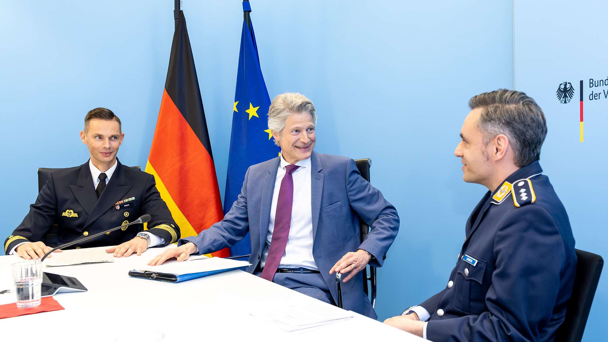Ein Soldat spricht mit einem Soldaten und einem Mann an einem Tisch sitzend